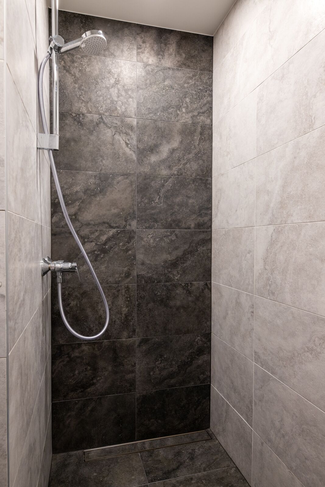 A shower with a handheld showerhead and a wall-mounted faucet.