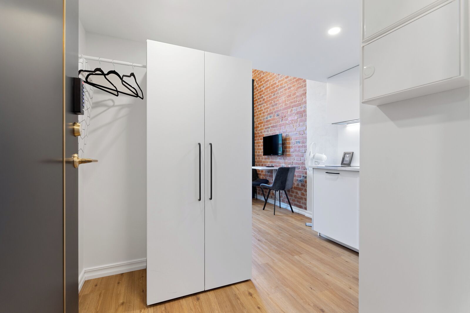 A modern kitchen with white cabinets, a brick wall, and a dining area with a chair and table.