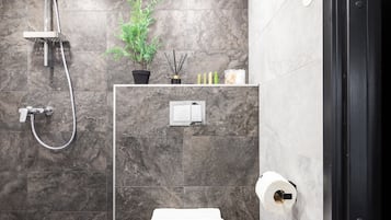 Uma casa de banho moderna com chuveiro, sanita e uma prateleira com produtos de higiene pessoal.