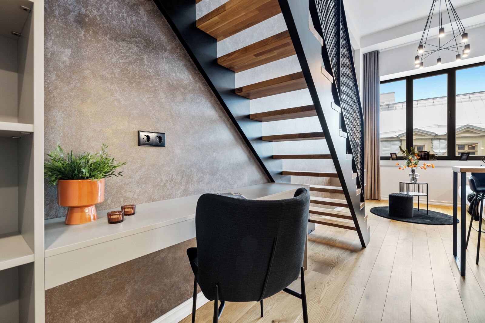 Un interior moderno con una escalera, una silla negra, una planta en maceta y una zona de comedor con vistas.
