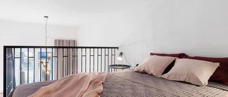 Un dormitorio moderno con una cama grande, una mesita de noche con lámpara y vistas a través de la barandilla de un balcón.