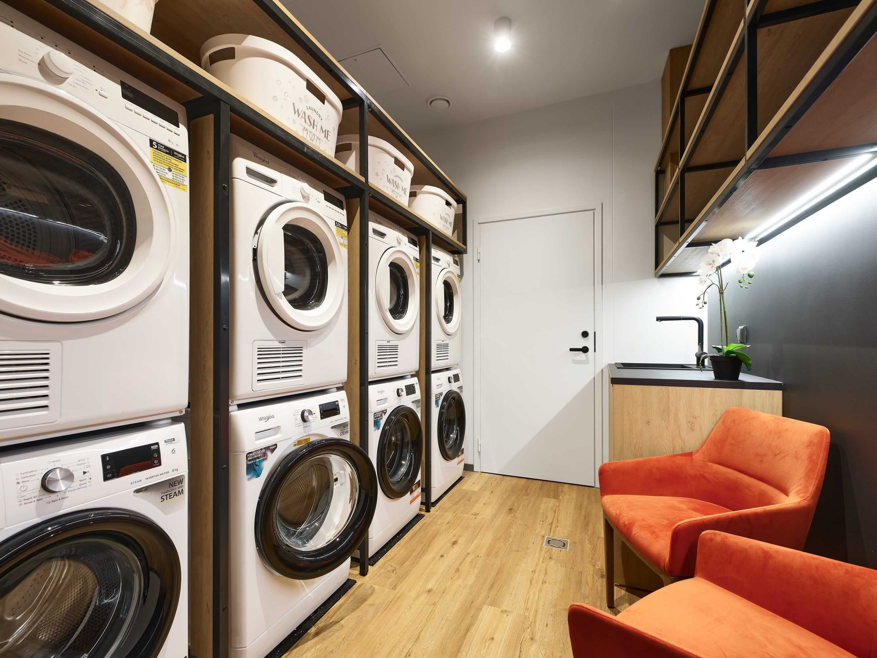 A laundry room with multiple washing machines, a sink, and a small seating area with orange chairs.