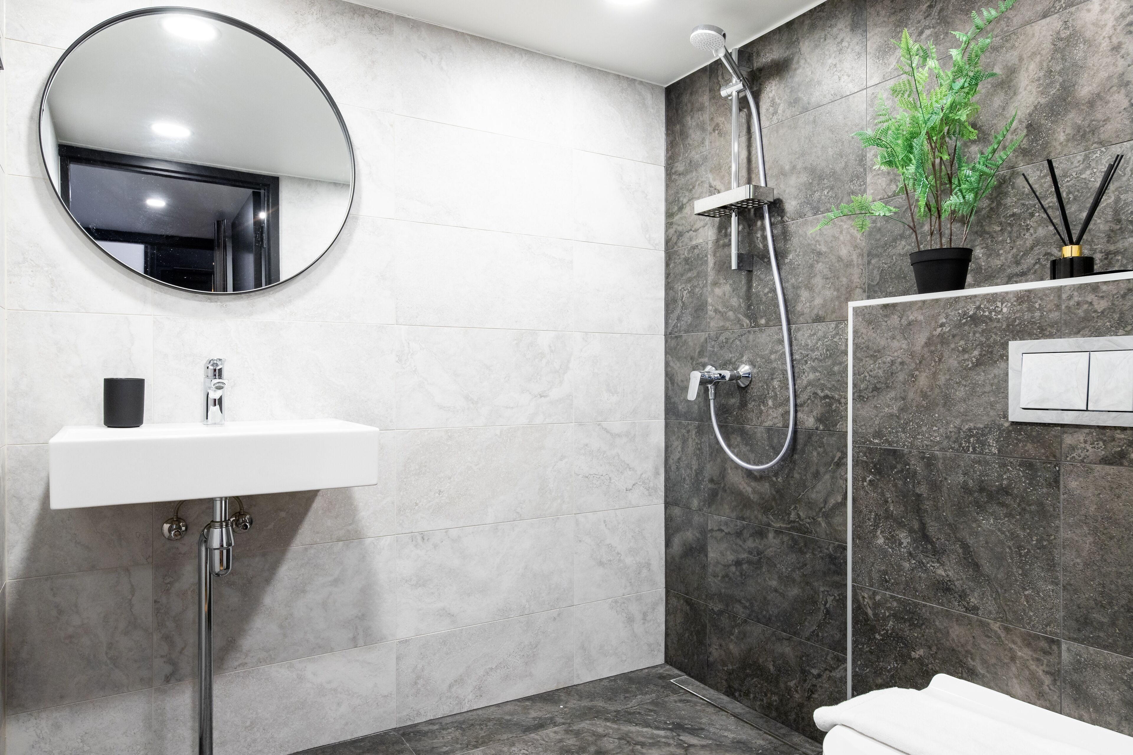 Un baño moderno con un espejo redondo, lavamanos blanco y una ducha con cabezal de ducha de mano.
