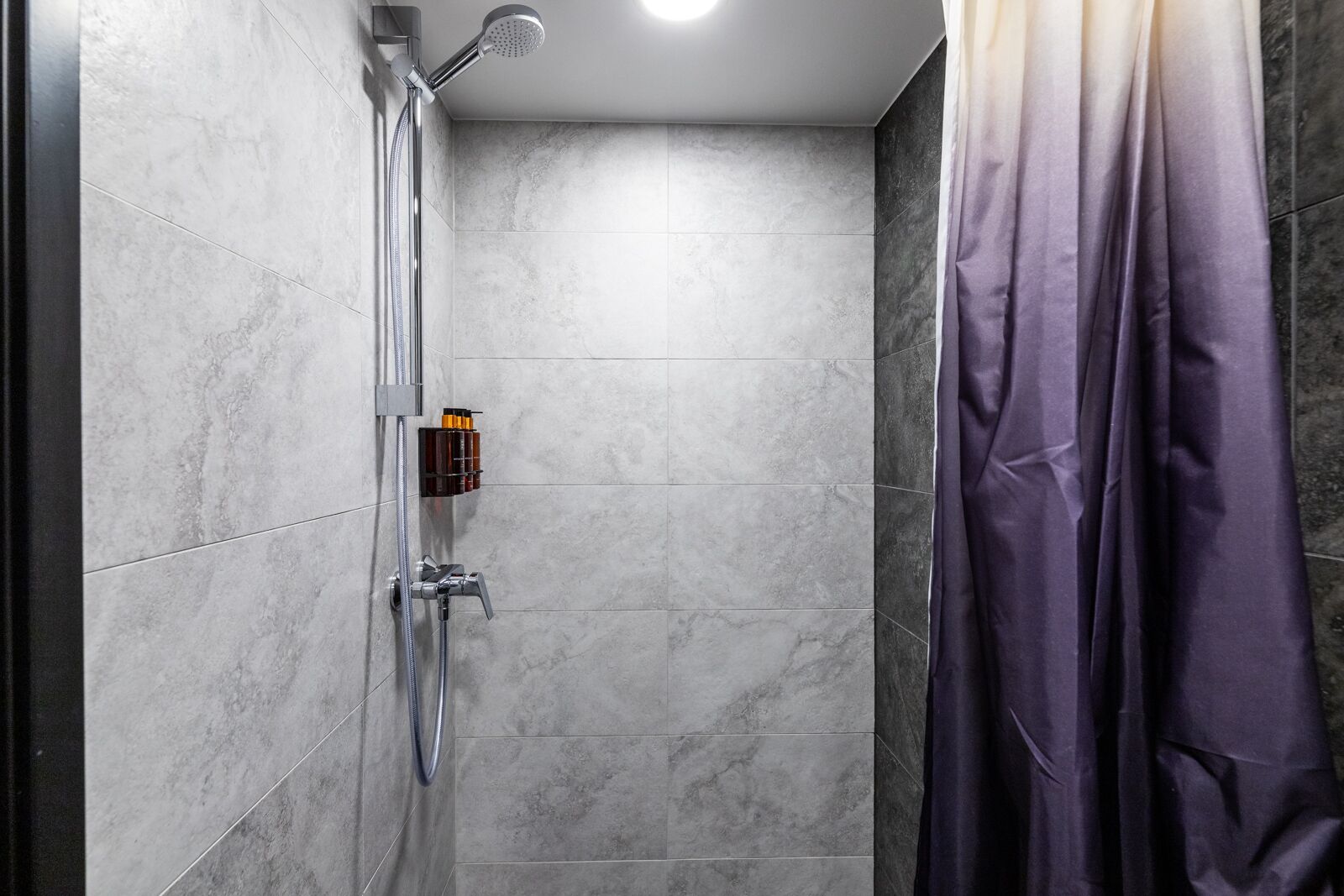 A modern shower with a handheld showerhead, a wall-mounted control panel, and a glass-enclosed shower area.
