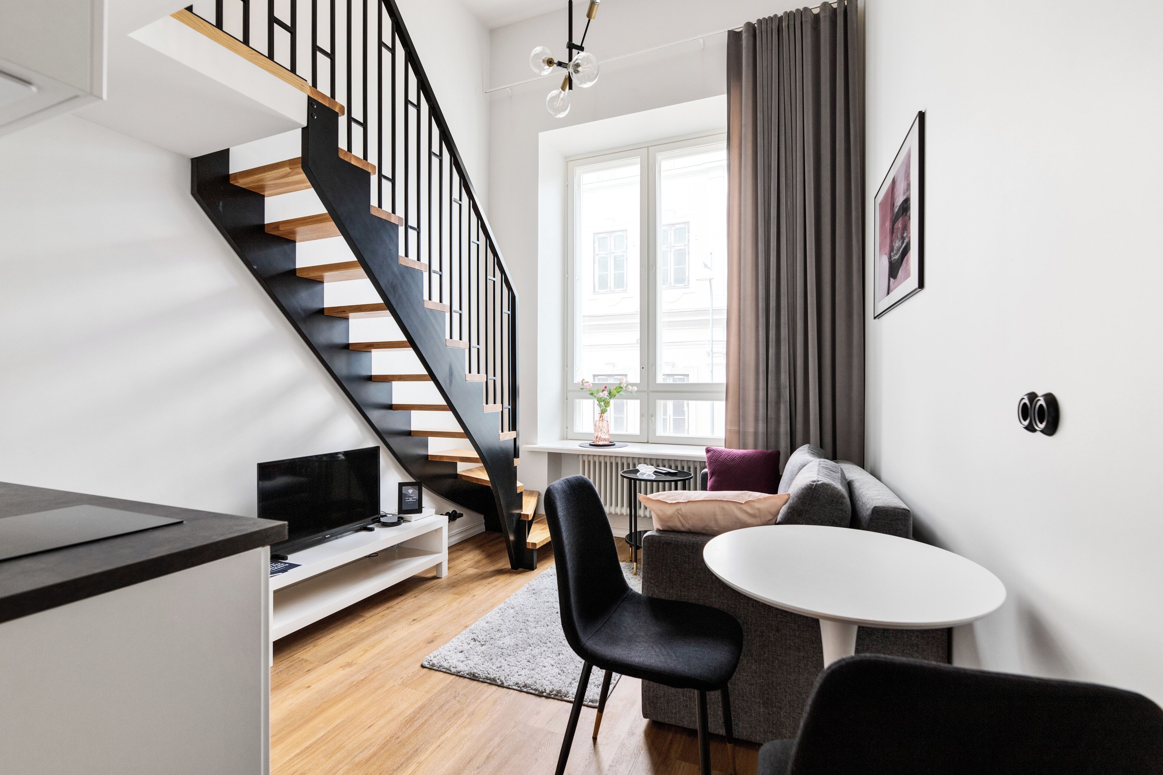 A modern living room with a staircase, a dining area, and a window with curtains.
