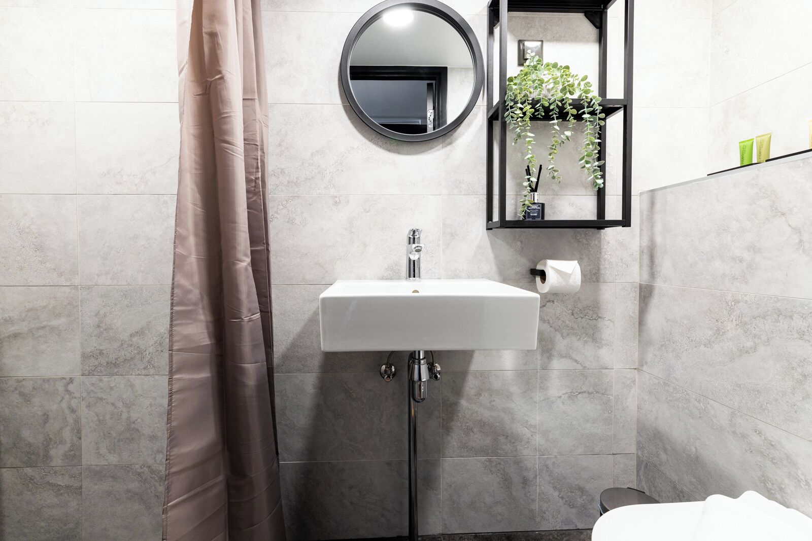 Ein Badezimmer mit einem weißen Waschbecken, einem runden Spiegel, einer Toilette und einer Duschvorhang.
