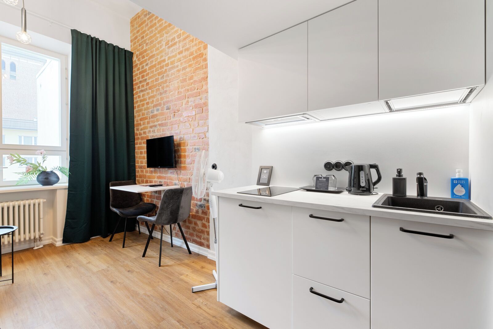 A modern kitchen with white cabinets, a black countertop, and a brick accent wall.