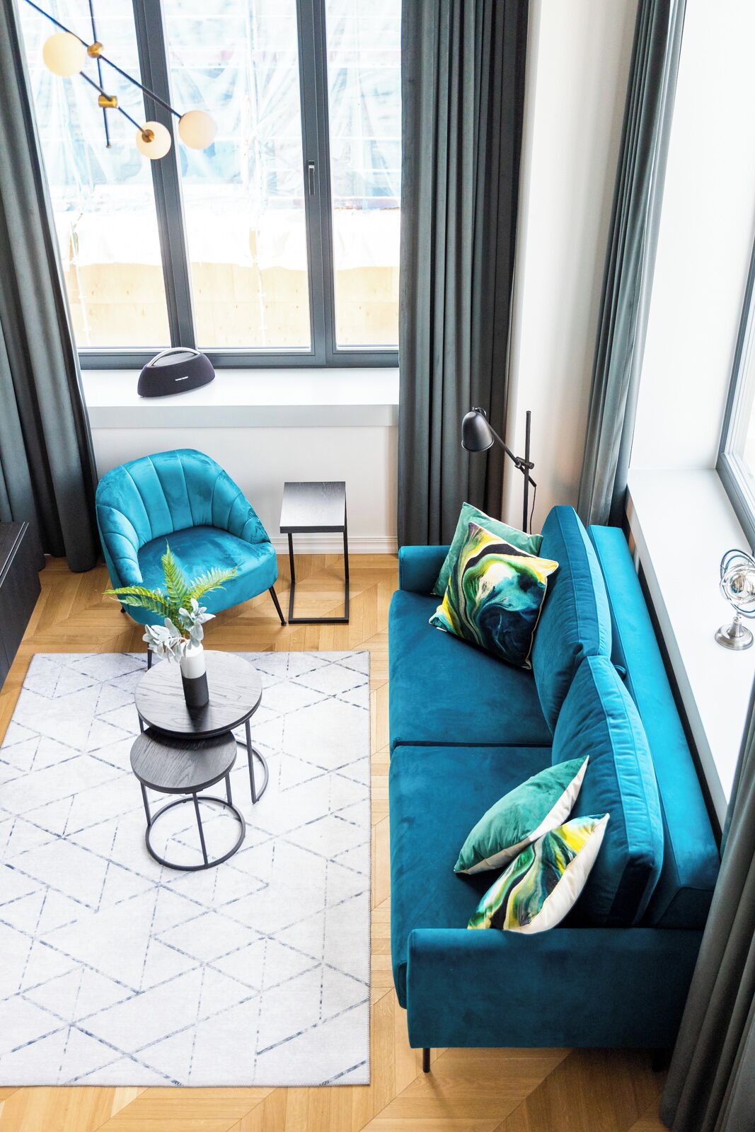A modern living room with a teal sofa, a blue armchair, a small round table, and a potted plant.