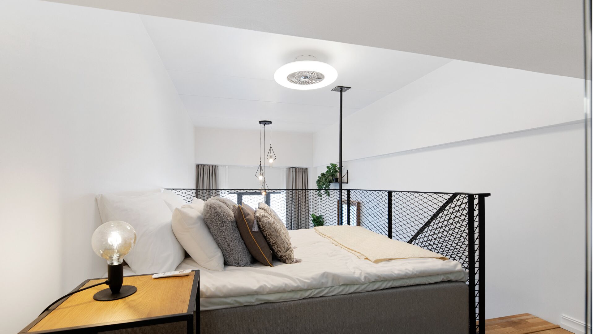 A modern bedroom with a bed, a bedside table with a lamp, a hanging light fixture, and a view of the living area through a balcony.