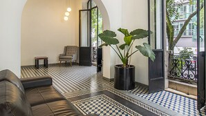 A modern living room with a black leather sofa, a patterned floor, a large potted plant, and a view through an open door. - Alure by Kukun (Mexico City)