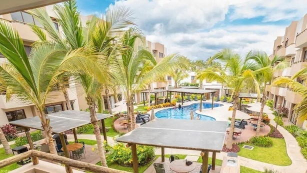 A hotel courtyard with a swimming pool, palm trees, and outdoor seating areas. - Departamentos Ambar (Mazatlán)
