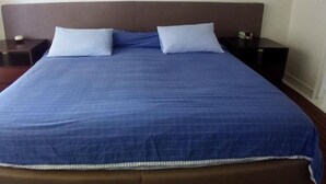 A large bed with a blue bedspread and two pillows, flanked by dark nightstands with a small item on each. - Departamentos Ambar (Mazatlán)