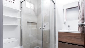 A modern bathroom with a glass-enclosed shower, a toilet, and a vanity with a mirror. - Departamentos Ambar (Mazatlán)
