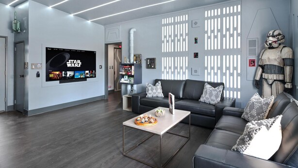 En moderne stue med en væg i Star Wars-tema, et stort fladskærms-tv, en lædersofa og en dekorativ statue.
