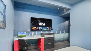 Et værelse med en væg i Star Wars-tema, et skrivebord med computer, en stol og en seng.
