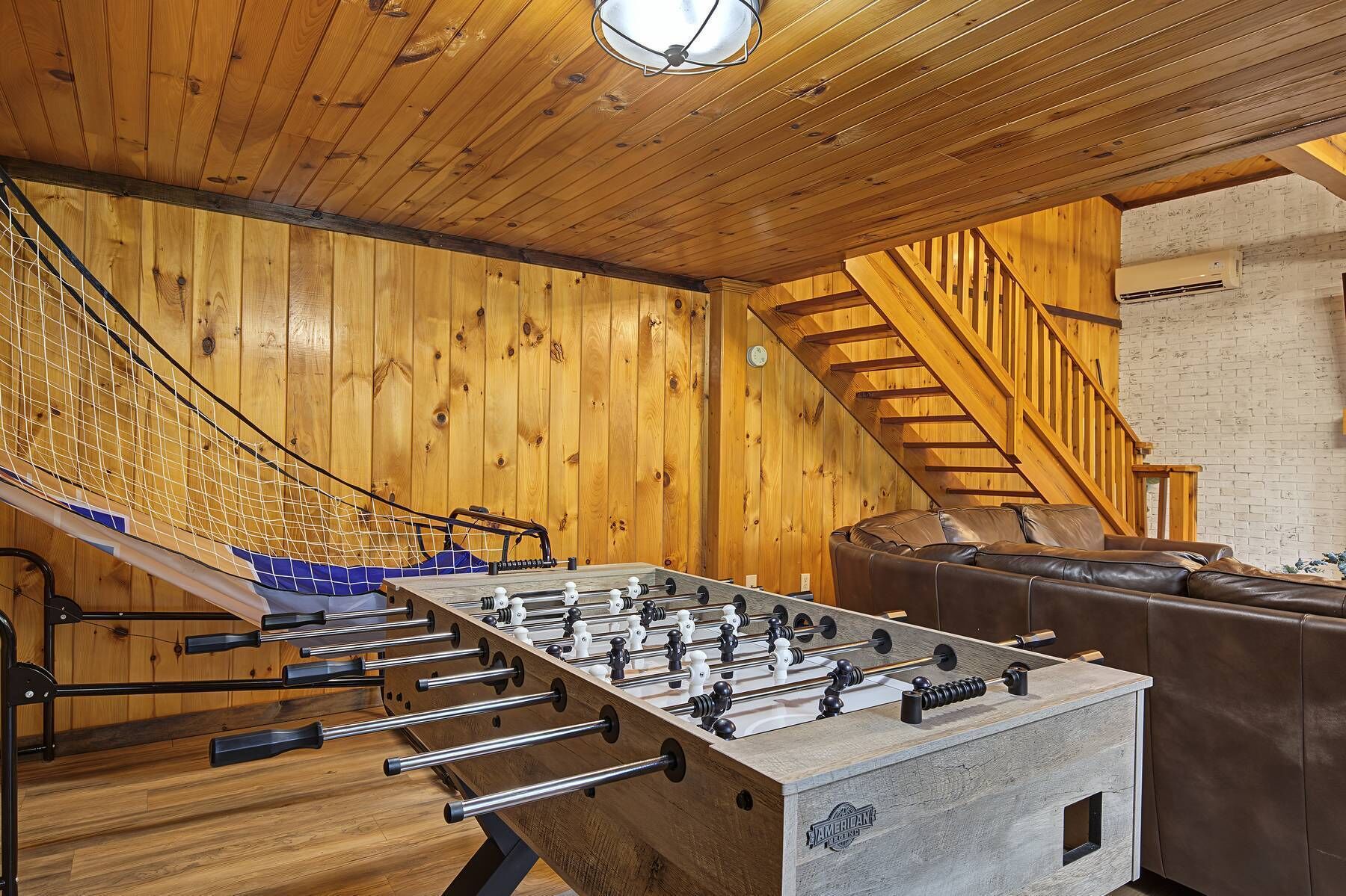 A wooden-floored room with a foosball table, a sofa, and a staircase.