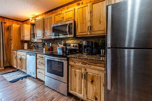 A kitchen with wooden cabinets, stainless steel appliances, and a granite countertop. - Large cabin near boat rentals & Nantahala with Hot Tub, Pool Table, & Gameroom (Bryson City)
