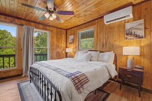 Une chambre à coucher comprenant un lit, une table de chevet, une lampe, un ventilateur de plafond et un appareil de climatisation.