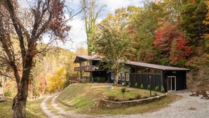 A two-story lodge with a stone foundation, a covered porch, and a gravel driveway leading to a wooden deck.