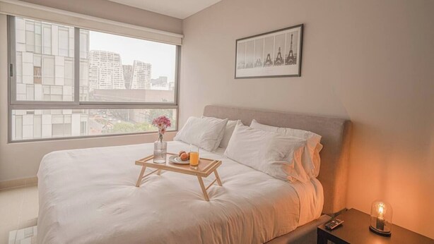 A hotel room with a large bed, a bedside table with a glass of orange juice, a vase with flowers, and a framed picture of the Eiffel Tower on the wall. - 1BR|1BA Apartment W/ pool, gym, high speed WiFi, located just a 3-minute walk from the new U.S. Embassy (Ciudad de México)
