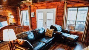 A cozy cabin-style room with a leather sofa, a wooden coffee table, and a plaid tablecloth. - Firefly Treehouse - Starlight Haven (Hot Springs)