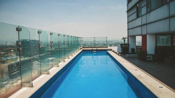 Une piscine sur le toit, dotée d’une paroi en verre et offrant une vue sur le paysage urbain.