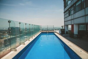 Piscina no terraço com barreira de vidro e vista para a paisagem urbana.