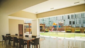 Un espace intérieur spacieux avec une grande table et des chaises, et un mur en verre donnant sur une aire de jeux à l’extérieur.