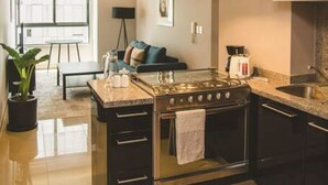 Une cuisine moderne équipée d’une cuisinière à gaz, d’un four et d’une hotte en acier inoxydable. On y trouve également un coin repas avec une table et des chaises, ainsi qu’une grande fenêtre qui laisse entrer la lumière naturelle.