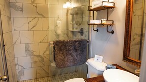 Un bagno con doccia vetrata, un water bianco, un mobile lavabo in legno con lavandino bianco e uno specchio con cornice in legno.