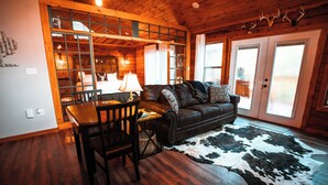 A cozy cabin interior with a dining area, a leather sofa, and a cowhide rug.