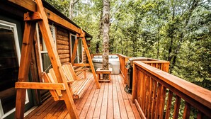 A wooden deck with a swing chair, a hot tub, and a grill.