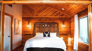A wooden cabin bedroom with a bed, a ceiling fan, and a window with curtains.