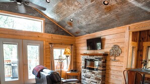 A spacious living room with a stone fireplace, wooden walls, and a ceiling fan. - Mountain Air Treehouse - Starlight Haven (Hot Springs)