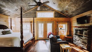 A log cabin bedroom with a four-poster bed, a fireplace, and a ceiling fan. - Mountain Air Treehouse - Starlight Haven (Hot Springs)