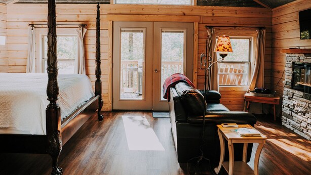 A rustic log cabin bedroom with a four-poster bed, a sofa, a small table, and a fireplace. - Mountain Air Treehouse - Starlight Haven (Hot Springs)