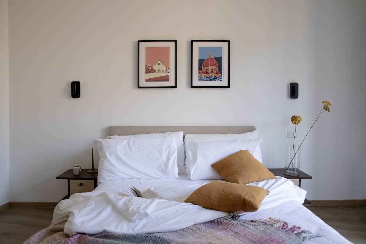 A neatly made bed with white and brown bedding, a small bedside table with a cup, and two framed pictures on the wall.