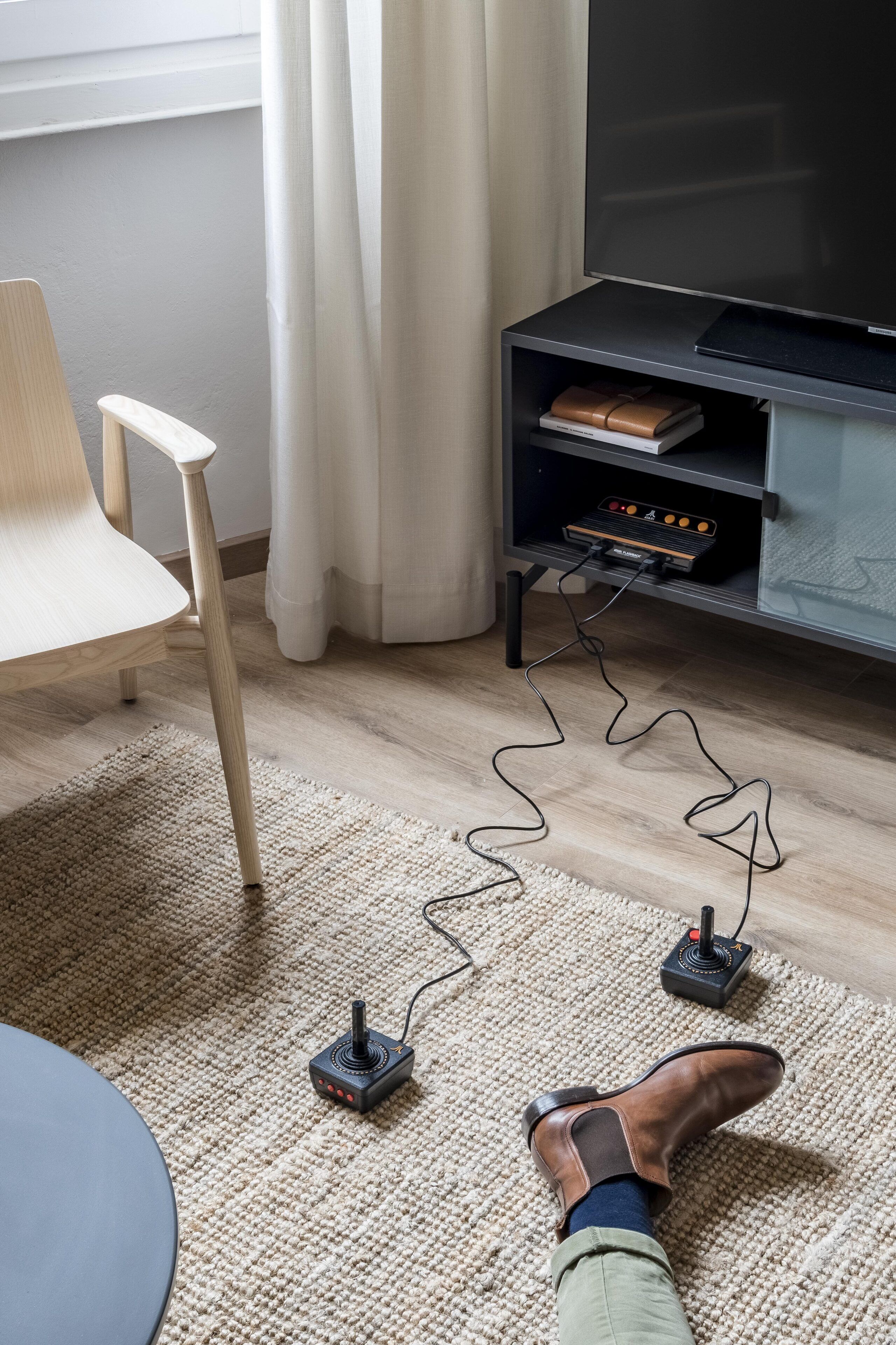 Ein Zimmer mit einem Holzstuhl, einer schwarzen TV-Konsole mit einem Flachbildfernseher und Füßen auf einem Teppich mit einer kabellosen Ladestation.