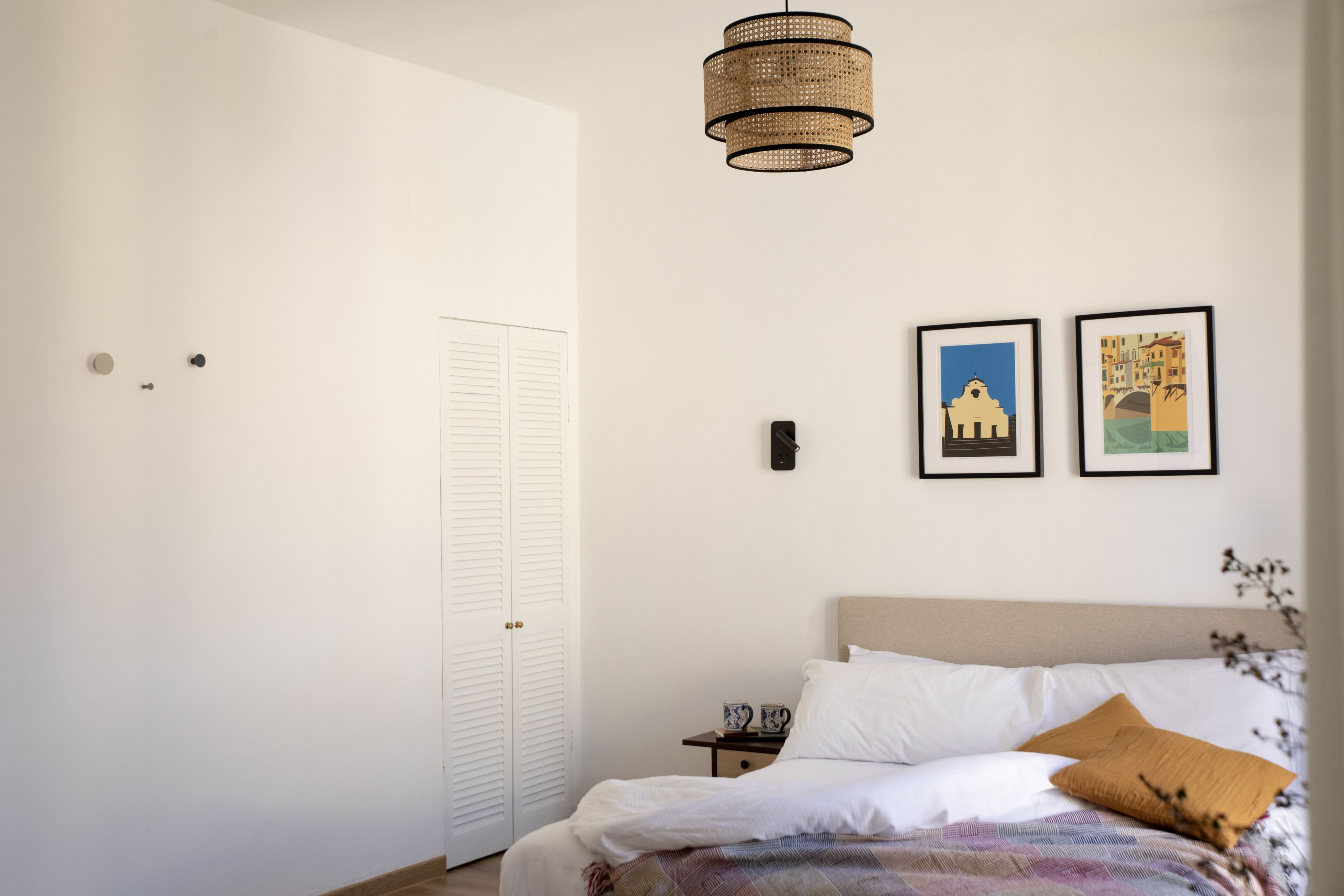 A bedroom with a bed, a nightstand, a wall-mounted lamp, and two framed pictures.