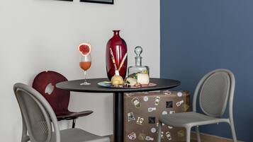 A dining area with a round table, two chairs, a red vase, a glass with a drink, and a cake.