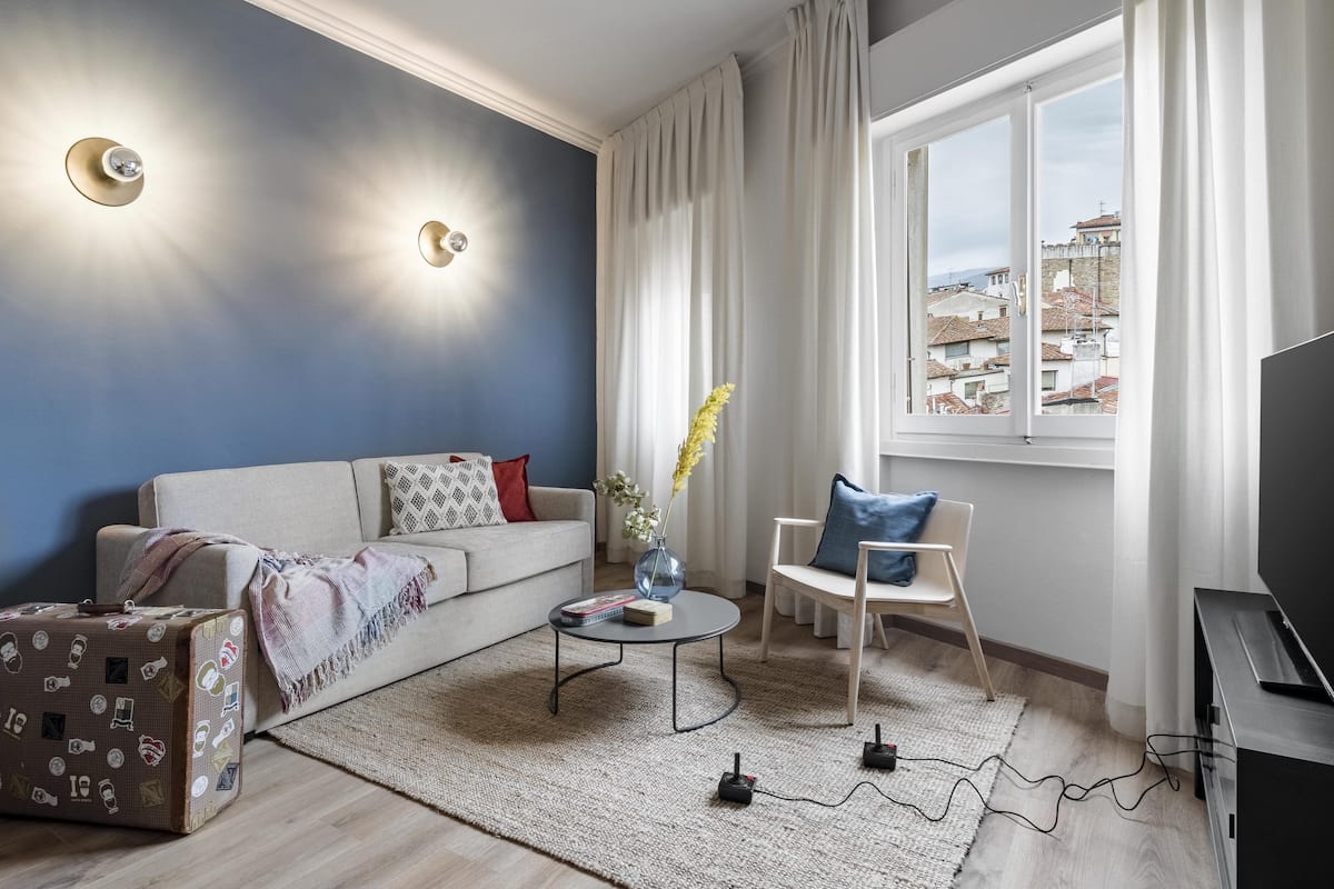 A modern living room with a sofa, a coffee table, a TV stand, and a window with a view of buildings.