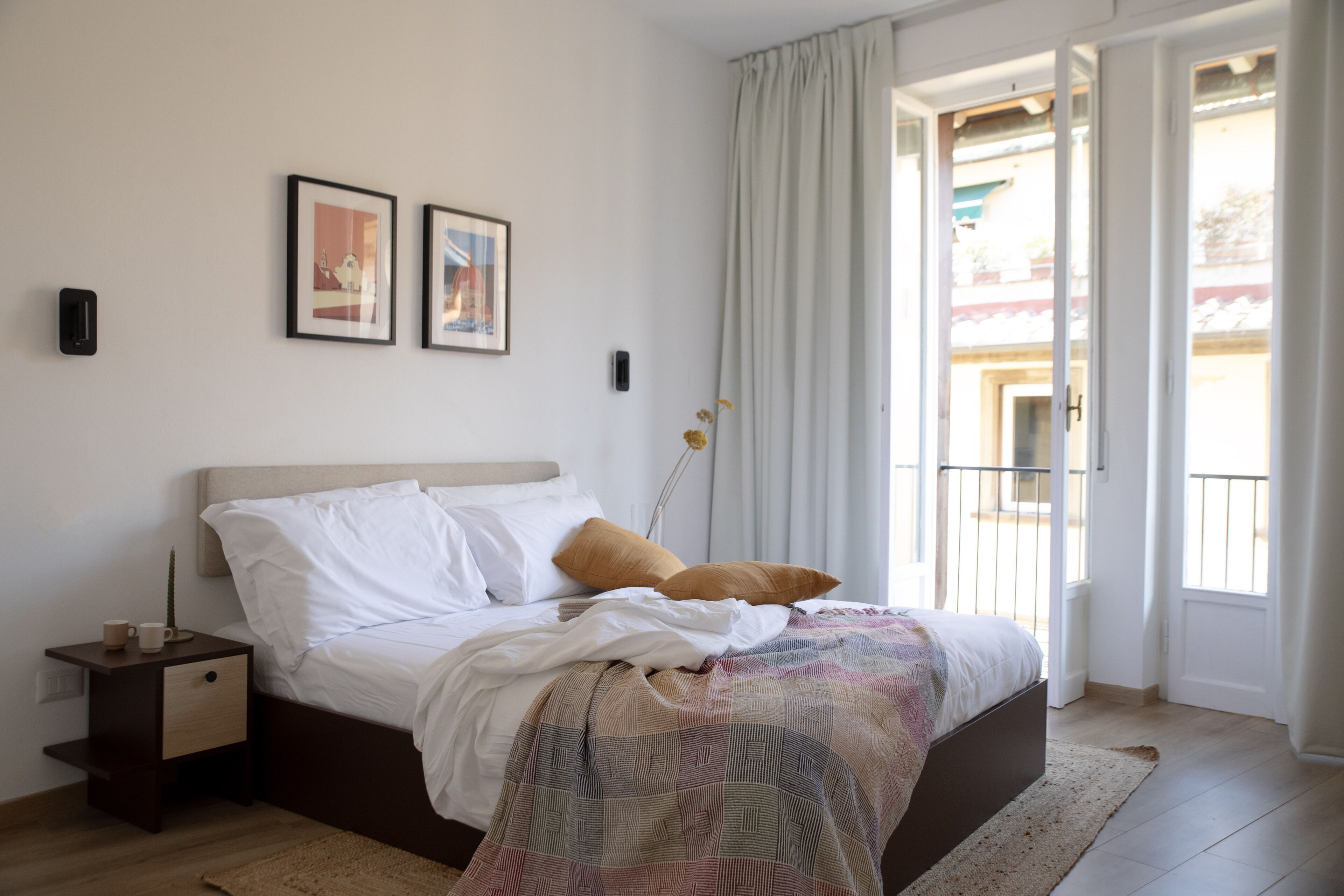 Una camera da letto con un letto, un comodino, una finestra con tende e due quadri appesi al muro.