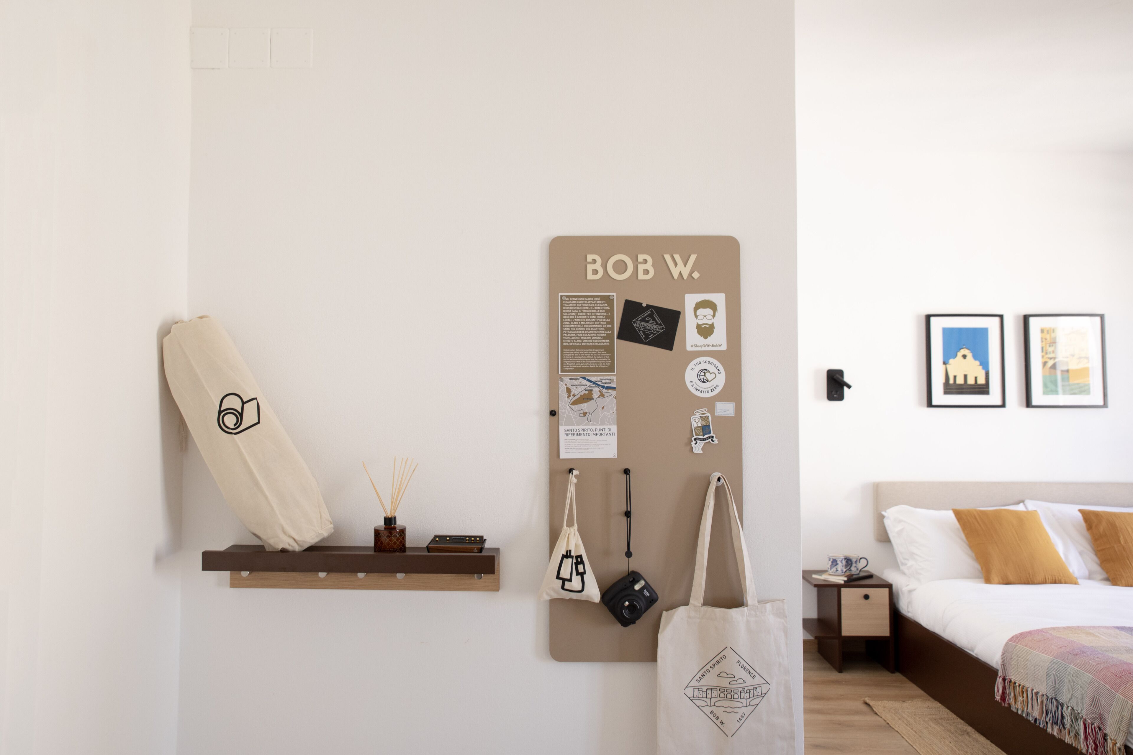 Een keurig opgeruimde slaapkamer met een bed, een prikbord aan de muur en een plank met een opgerolde voorwerp en een kleine vaas.