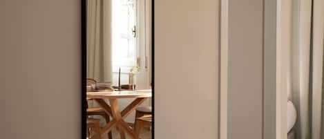 Una habitación con mesa y sillas de madera, una lámpara colgante y vistas por una puerta a un espacio exterior con ventana y cortinas.