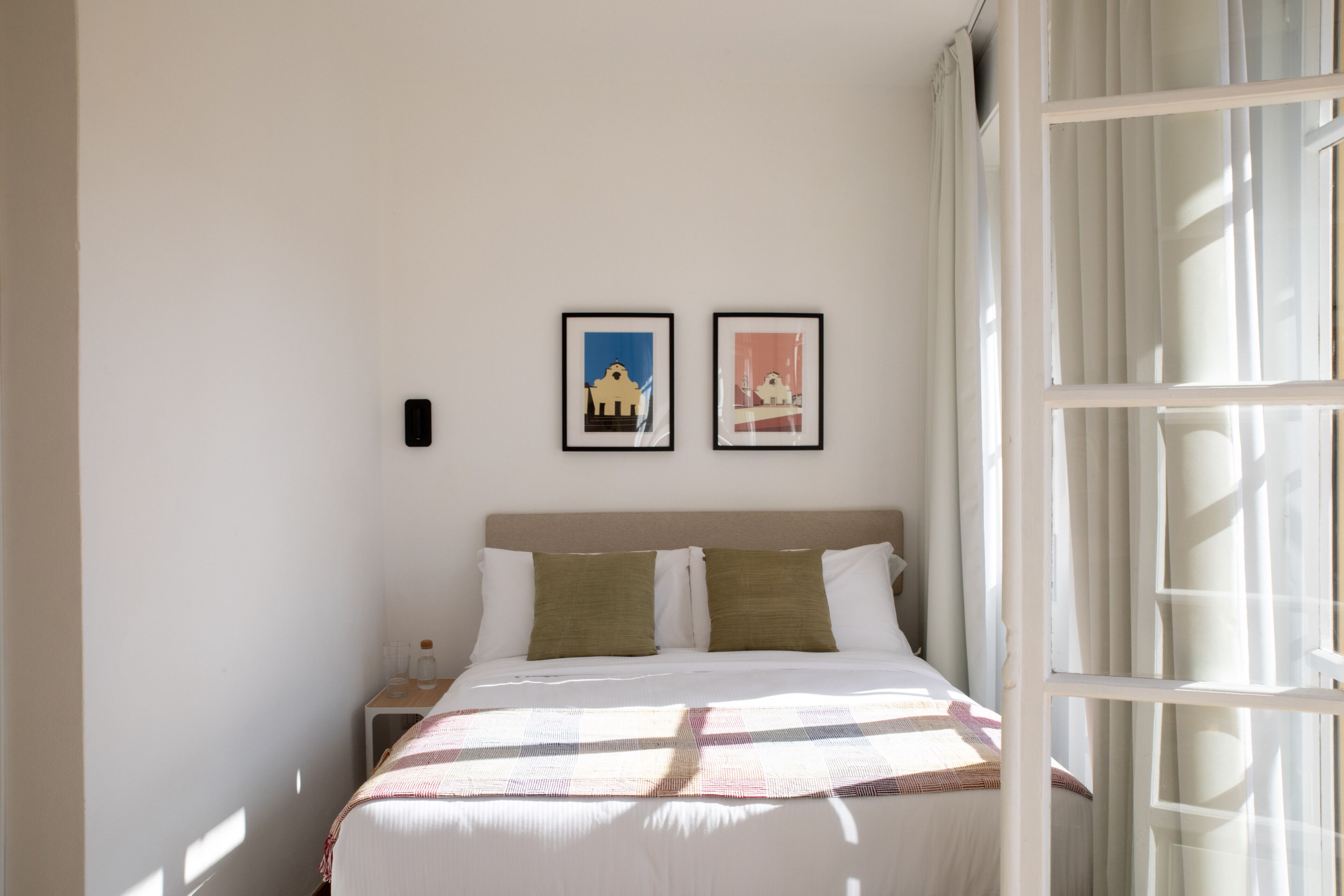 A neatly made bed with a checkered bedspread, two pillows, and a nightstand with a bottle and glasses.