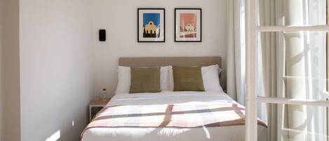 Una cama bien hecha con un edredón a cuadros, dos almohadas y una mesita de noche con una botella y vasos.