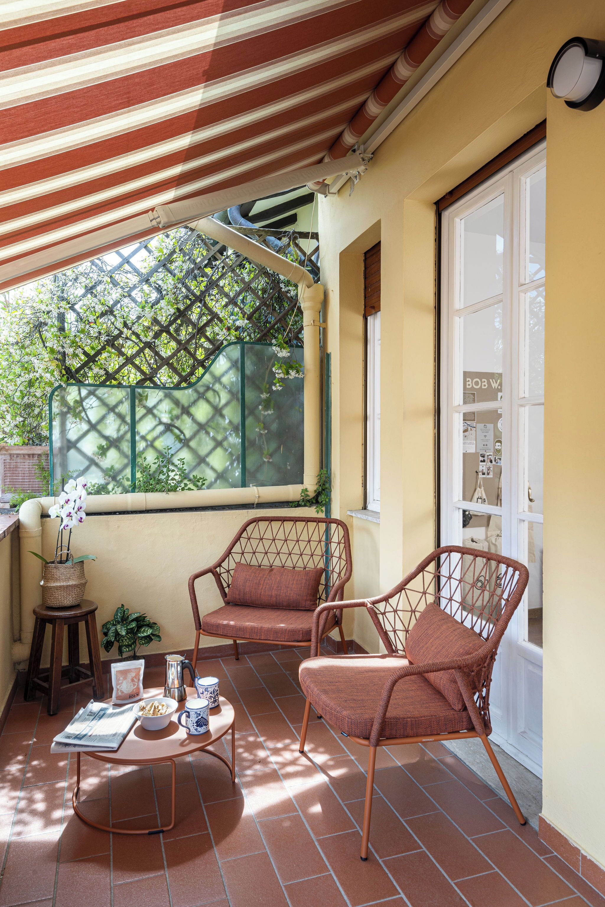 A sunlit patio with two wicker chairs, a small round table, and a potted orchid.
