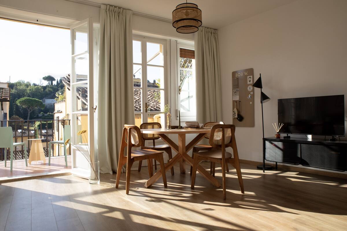 A spacious living room with a wooden dining table, chairs, and a TV.