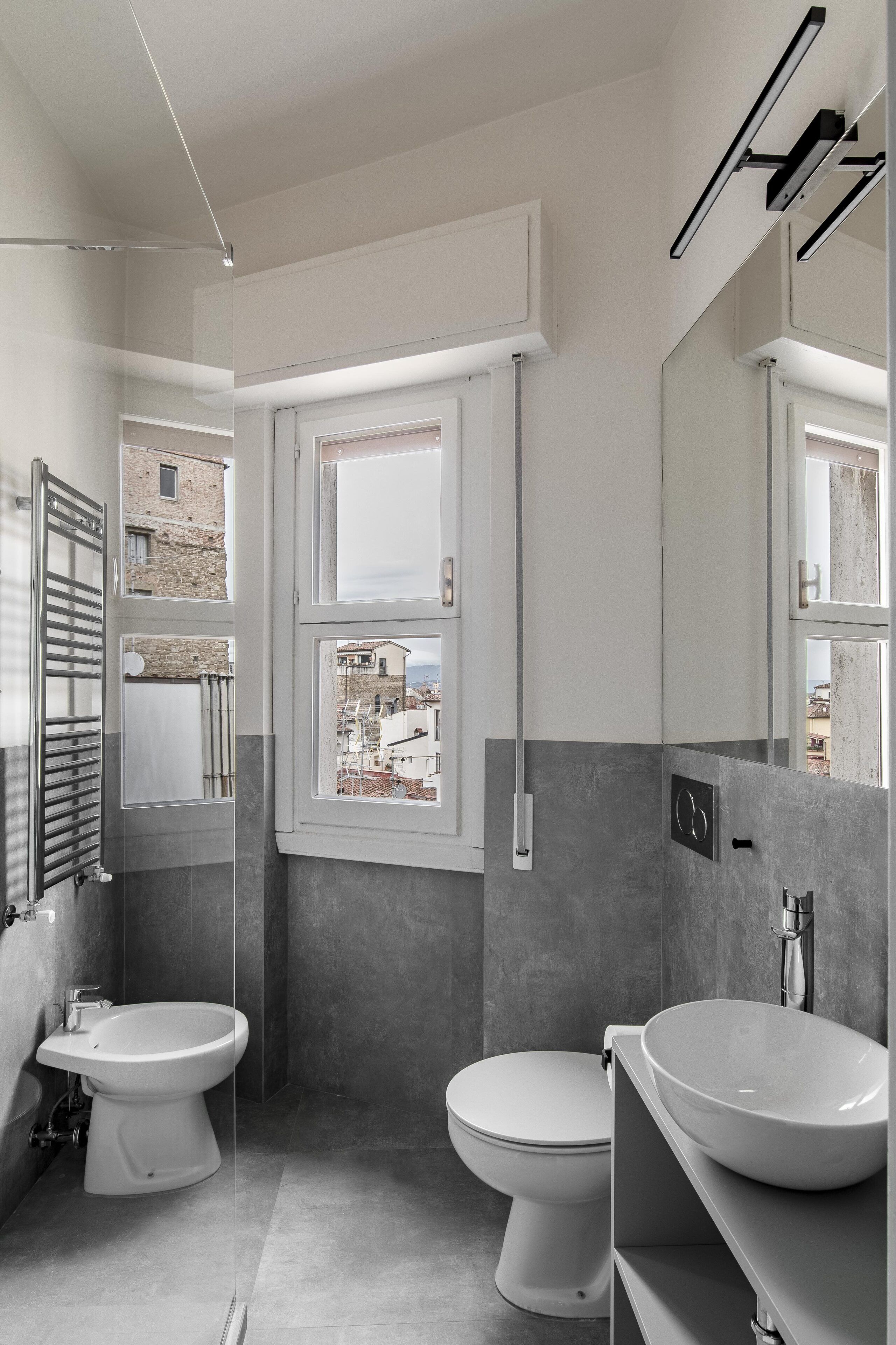 Bany modern amb bidet, vàter i rentapel. Hi ha una finestra que deixa entrar llum natural i ofereix vistes a edificis.