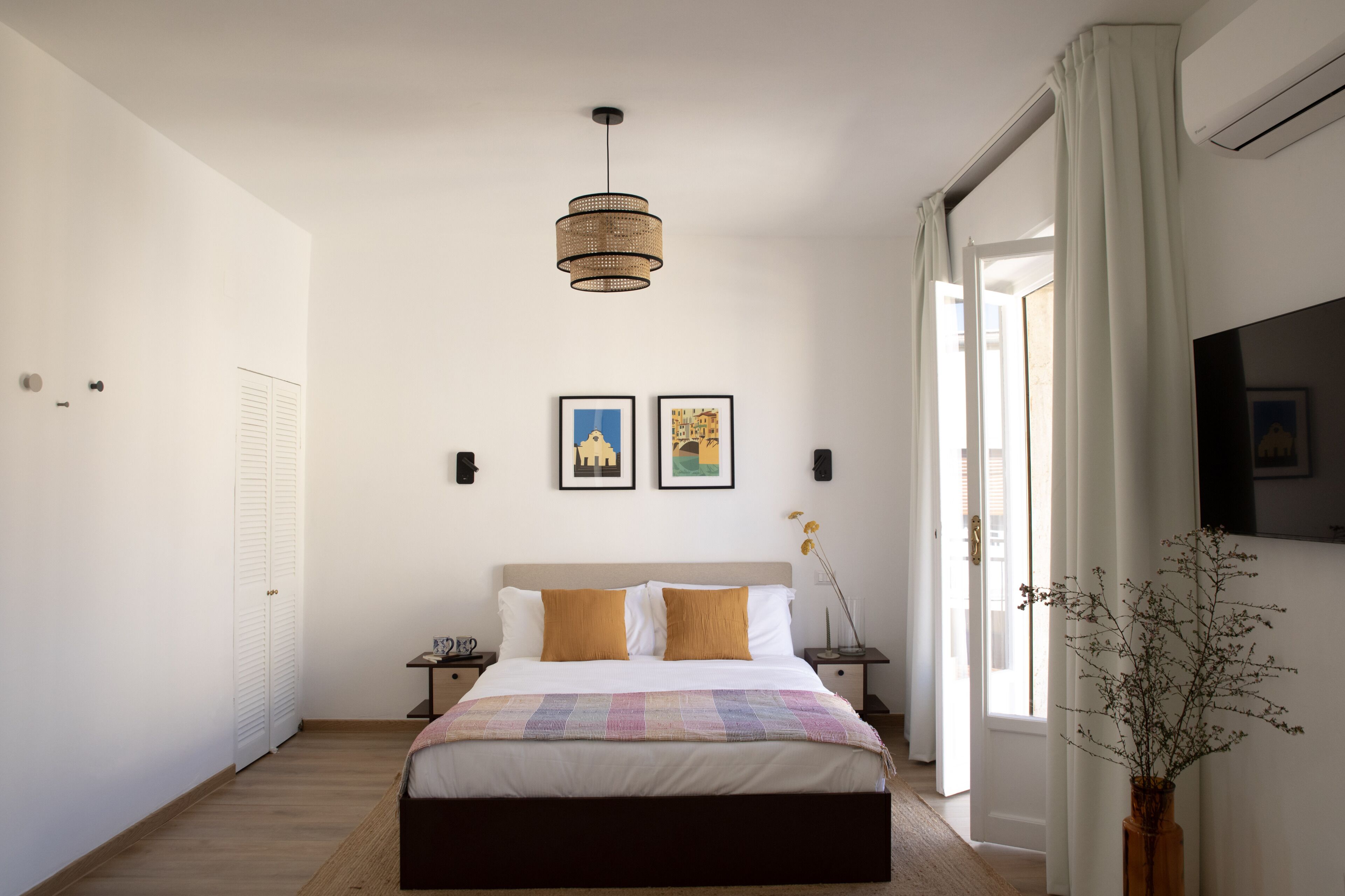 Une chambre à coucher comprenant un lit, des tables de chevet, un luminaire suspendu et une fenêtre avec des rideaux.